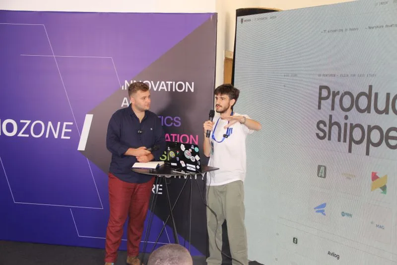 Two speakers on the Future 2 Tech stage, one holding a microphone, in front of an innovation backdrop.