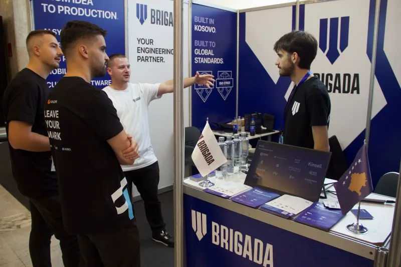 Visitors talking with the Brigada team at the stand, with Your engineering partner and Built in Kosovo printed on the walls.