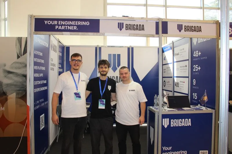 Three members of the Brigada team in white Brigada shirts standing in front of the Brigada stand at Future 2 Tech 2026.