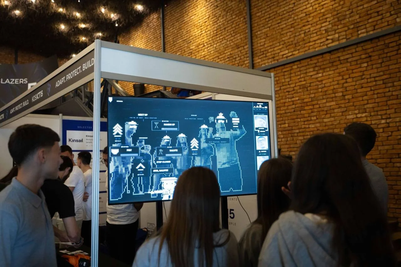 A crowd watching the interactive Brigada game on a large screen at the booth.