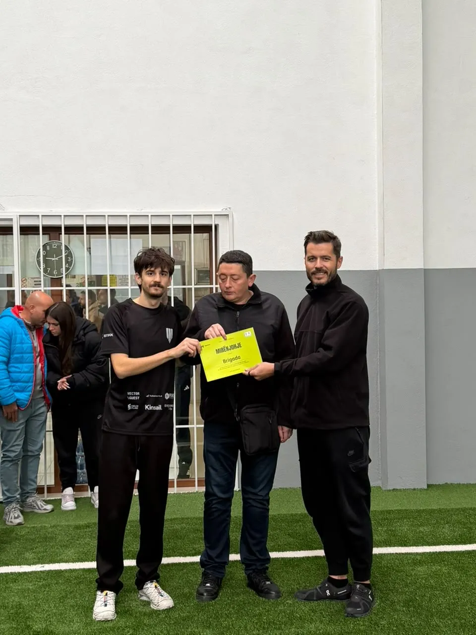A Brigada player receiving a yellow certificate of recognition, "Mirënjohje", addressed to Brigada, from two organisers.